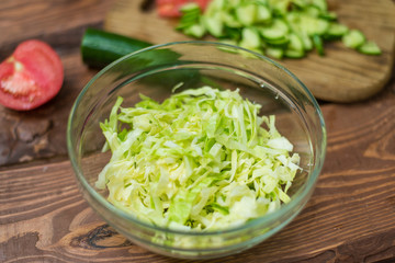 Chopped fresh green cabbage in a glass bowl on a wooden background. Cooking healthy, healthy, vegetable salad.