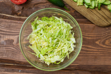 Chopped fresh green cabbage in a glass bowl on a wooden background. Cooking healthy, healthy, vegetable salad.