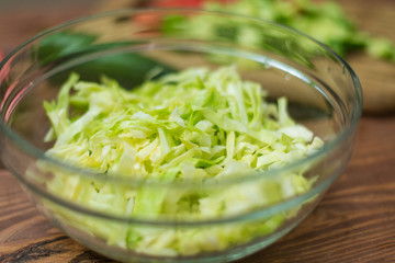 Chopped fresh green cabbage in a glass bowl on a wooden background. Cooking healthy, healthy, vegetable salad.