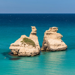 Naklejka premium The bay of Torre dell'Orso, with its high cliffs, in Salento, Puglia, Italy. Turquoise sea and blue sky, sunny day in summer. The stacks called the Two Sisters. A person swims in the clear water