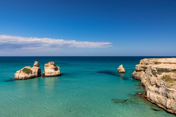 Fototapeta premium The bay of Torre dell'Orso, with its high cliffs, in Salento, Puglia, Italy. Turquoise sea and blue sky, sunny day in summer. The stacks called the Two Sisters, immersed in the sea.