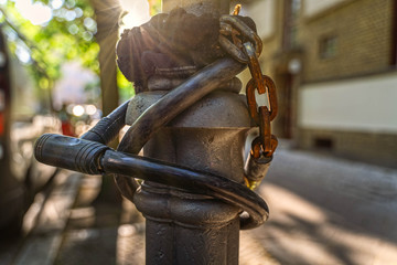 Lamppost with rusty bicycle locks, blurred urban background with sun rays