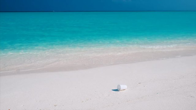 White plastic cap lies on the perfect sandy beach. Plastic trash pollutes the pristine sea and the tropical beach