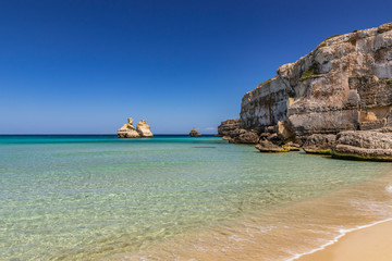 Fototapeta na wymiar The bay of Torre dell'Orso, with its high cliffs, in Salento, Puglia, Italy. Turquoise sea and blue sky, sunny day in summer. A beach of fine white and pink sand. The stacks called the Two Sisters.