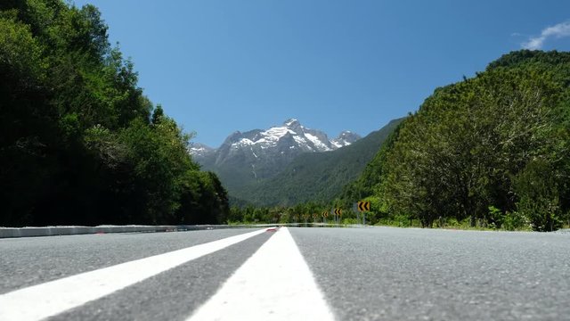 Camera moves over the asphalt road with snow capped mountains on the background. Chilean Patagonia near the town of Chaiten