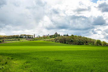 Eye-catching landscape with green grass, trees and monastery up the hill under cloudy sky