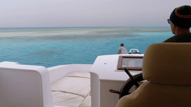The captain controls the tourist yacht on the white sandy island in the sea near the reef