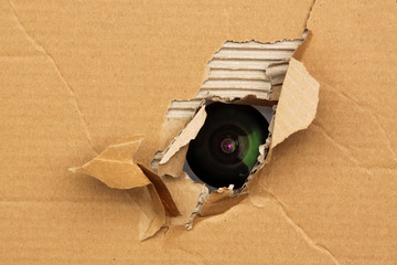 Camera lens looks out of the hole in the cardboard, the concept of surveillance, peeping