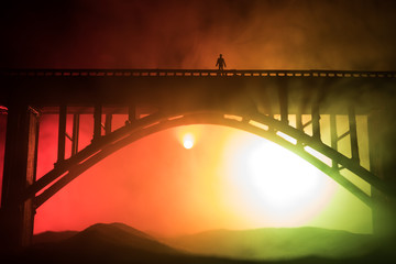 Obraz premium Artwork decoration. Silhouette of powerful metallic bridge at night with foggy backlight. Silhouette of person standing on bridge.