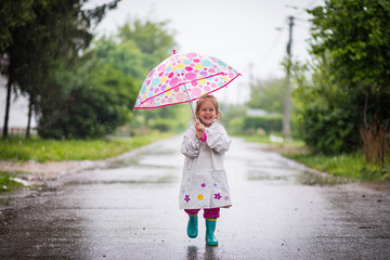 Happy child playing in the rain. Little girl with umbrella having fun outdoor .