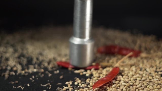 A mix of Indian seeds is being crushed by a pestle in a studio and close-up view. Cooking, decoration, art concept.