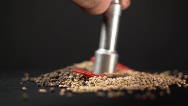 A mix of tasty Indian seeds and red chili are being crushed by an iron pestle in close-up view. Decoration, cooking, kitchen equipment concept.