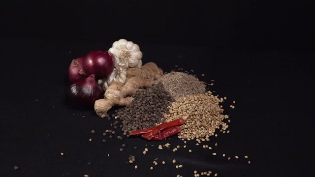 Pictorial group of Traditional Indian spices and vegetables in a studio while the camera is receding. Chili, cumin. white/black pepper, onion, ginger.