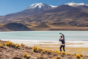 Fototapeta na wymiar Landscape woman photographer taking selfies in an amazing wilderness environment at Atacama Desert Andes mountains lagoons. A woman cut out silhouette over the awe Tuyajto Lagoon scenery at Altiplano