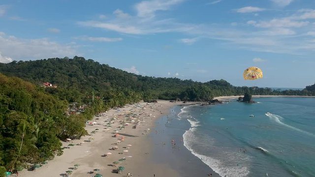 Aerial dolly forward of people relaxing and parasailing in Manuel Antonio National park beach, Costa Rica.