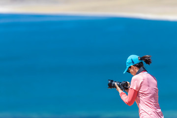 Landscape woman photographer taking photos in an amazing wilderness environment at Atacama Desert Andes mountains lagoons. A cut out silhouette over the blue waters with a mirror less camera shooting