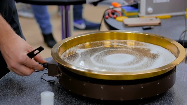 Sound vibration transforms white sand particles on steel surface at technology futuristic exhibition. Science, resonance and physics concept
