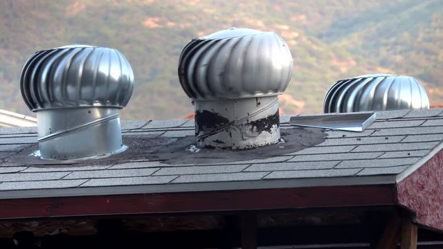 Three metal ventilator turbines on a shingle roof quickly rotate on a hot and windy day.