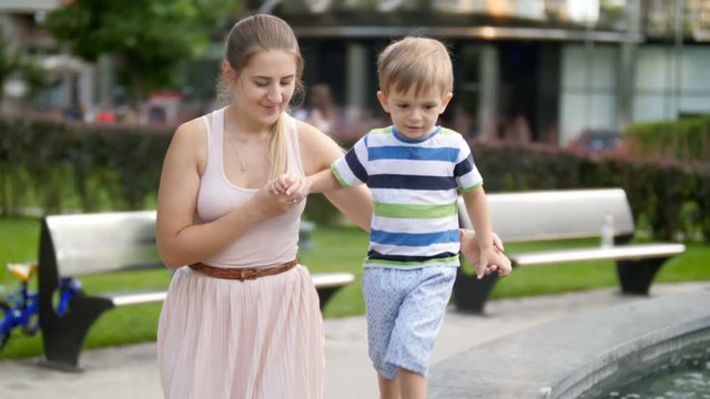 4k footage of little todler boy holding his mother by hand while walking on high parapet at park