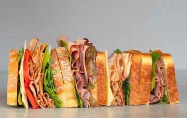 Freshly made deli style sandwich with lettuce, several different kinds of vegetables, tomatoes, cheese, meats similar to ham, chicken or turkey.