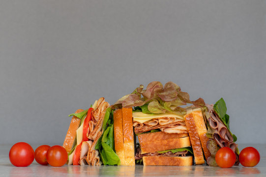 Freshly made deli style sandwich with lettuce, several different kinds of vegetables, tomatoes, cheese, meats similar to ham, chicken or turkey.