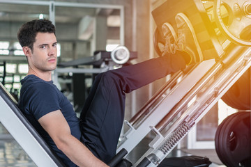 Handsome man lowering weight training legs on leg press machine and working out in the fitness gym