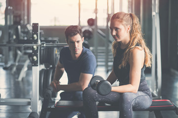 Young woman sitting on a stool with personal trainer, Trainer making fitness for female client at gym