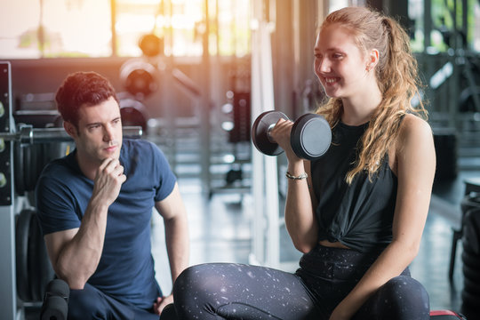Young woman sitting on a stool with personal trainer, Trainer making fitness for female client at gym