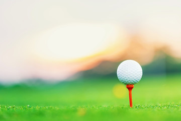 golf ball on tee at 1st hole tee off with blur green grass foreground and blur colorful sky with silhouette trees background during sunrise, Thailand