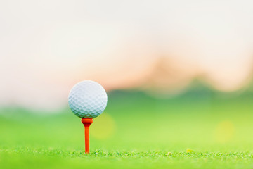 golf ball on tee at 1st hole tee off with blur green grass foreground and blur colorful sky with silhouette trees background during sunrise, Thailand