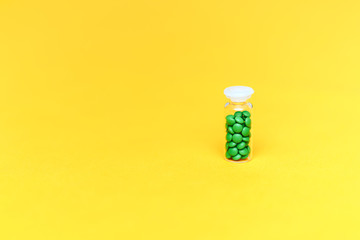 Medical green pills in a glass bottle on yellow background copyspace, health