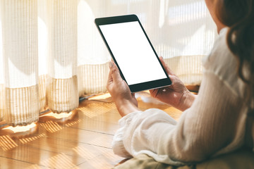 Mockup image of a woman holding black tablet pc with blank white desktop screen while laying down on the floor with feeling relaxed