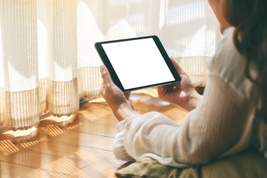 Mockup image of a woman holding black tablet pc with blank white desktop screen while laying down on the floor with feeling relaxed