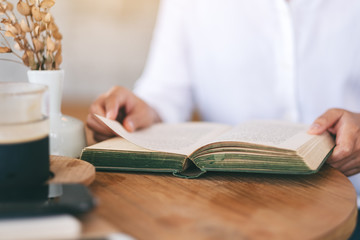 Closeup image of a woman holding and reading a vintage novel book on wooden table