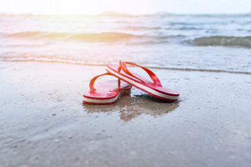 Red flip flops on beach with sandy beach sea ocean and sunlight background