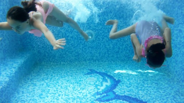 4k video of two teenage girls diving underwater at indoor swimming pool. Children having fun and enjoying water