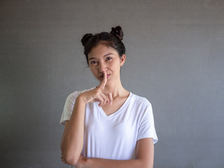 Emotional beautiful lovely woman with attractive appearance, keeps fore finger on lips, demonstrates silence gesture, ask to keep confidential information in secret, poses against gray wall. 