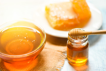 Honey in jar with wooden dipper and honeycomb on white plate on table background