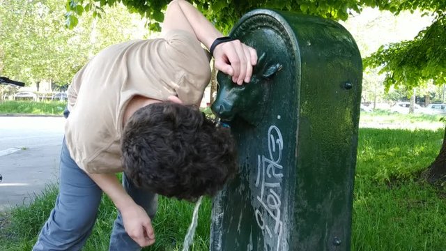 A young Caucasian boy drinks from a public drinking fountain in Turin, Italy. The fountain represents the head of a bull, symbol of the city. 25 fps