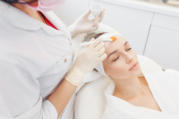 Obraz na płótnie Canvas Beautician smears the skin with a rejuvenating serum of the face of her client woman with a brush. The concept of modern anti-aging procedures in the beauty salon
