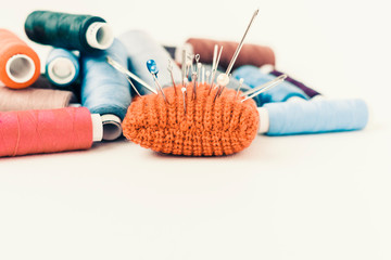 Red knitted needle pad for sewing and colored thread coils on white background with copy space for...