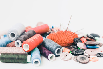 Red knitted needle pad for sewing, sewing buttons and colored thread coils on white background with...