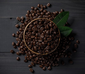 Coffee beans and coffee leaves in the bowl on the wooden table