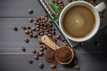 Hot coffee cup with coffee beans and the ground powder of coffee on the wooden table