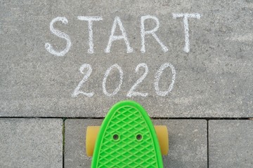 Start 2020 written in chalk on gray sidewalk, skateboard before the text.