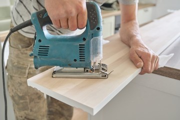 Close-up of carpenters hand using professional woodworking electric tools when working with wood. Male carving hole in wooden panel board, carpentry, woodwork, profession, people
