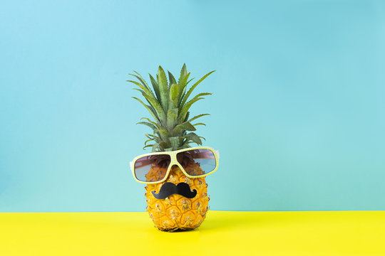 Yellow ripe pineapple in sunglasses with black mustache yellow blue background. Funny face from tropical fruit. Concept