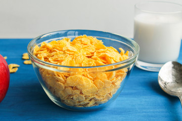  Breakfast cereal with a glass of milk. Apple and spoon on blue background