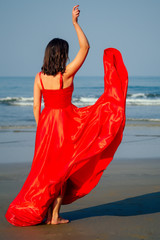 Beautiful woman standing on a cliff over blue sky and Goa sea. Brunette girl in red silk dress copyspace