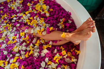 cropped shot of barefoot woman with flowers, candles, colorful sea salt and bath for nails in beauty salon in Bali hotel tropical vacation.depilation epilation shugaring hair removal concept